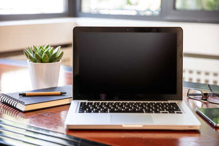 Computer screen mockup. Laptop with black blank screen on a wood desk, office background, copy spaceの写真素材