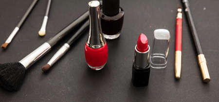 Make up cosmetics products in red and black. Red lipstick and nail polish, eye pencil and brushes against black color backgroundの写真素材
