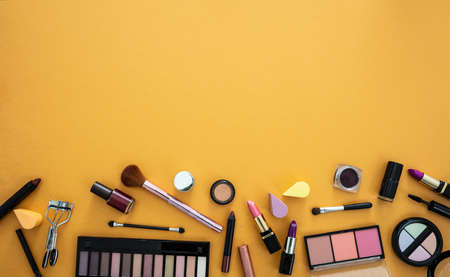 Make up cosmetics flat lay. Lipstick and nail polish, eye shadows and blush, brushes and pencils against yellow orange color background, copy space.の写真素材