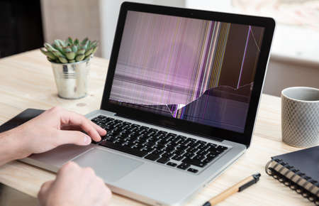Broken laptop repair, insurance concept. Man working with a computer with damaged screen, office business background.の写真素材