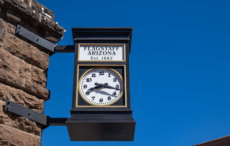 Flagstaff, Arizona, USA. May 25, 2019. A street analog clock, on a stone building is the timekeeper for the citizens. A vintage, metal, round watch under America's clear blue sky. Space, empty.のeditorial素材