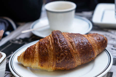 Coffee and croissant. A well-done butter croissant on white dish in close up view. Blur cup on a...