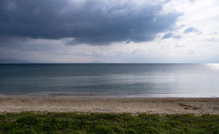 Heavy, fluffy clouds background meet calm dark blue sea far from the sandy coast. Orange buoys and a...