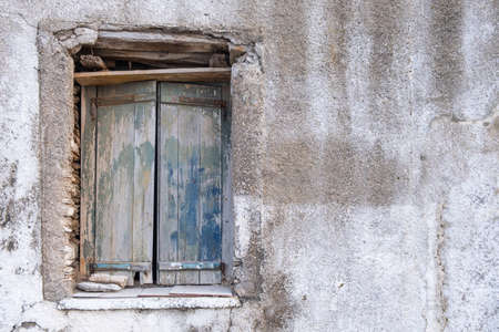 Old double closed wooden shutters. Rusty hinges on peeled planks,  stones keep the window shut. Wall...