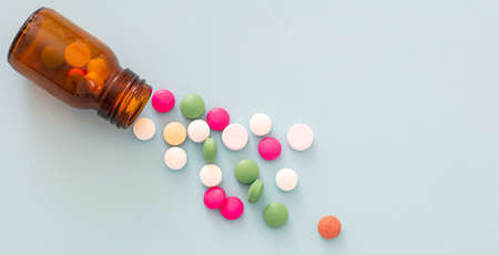 Medicine pills scattered out of a glass bottle on blue background. Pharmacy pills top view. Medical...