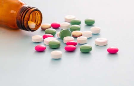 Medicine pills scattered out of a glass bottle on blue background. Pharmacy pills closeup view. Medical treatment, health conceptの写真素材
