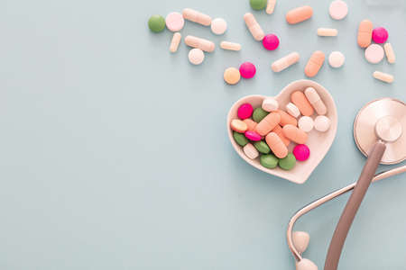Heart disease treatment. Pills, tablets capsules and stethoscope on blue pastel background. Colorful...