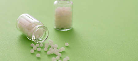 Homeopathy concept. Homeopathic globules out of a glass bottle, green background. Alternative herb...