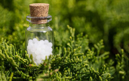 Homeopathy concept. Homeopathic globules in a glass bottle, green nature background. Alternative herb medicine healtcare pills, copy spaceの写真素材