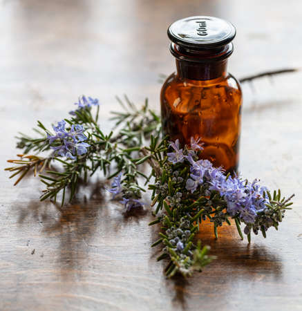 Rosemary herbal medicine. Glass bottle and fresh blooming twig on a wooden table, Essential oil, cosmetics, perfume container. Alternative medication concept.の写真素材