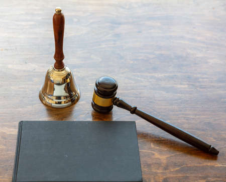 Law theme. Judge gavel and bell, a black blank legal book on wooden desk background, copy space. Auction, court tableの写真素材