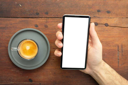 Mobile phone screen mockup. Man holding a smartphone with blank white screen, wooden background,...