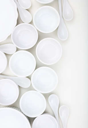 Dishware concept. White empty porcelain bowls and teaspoons background. Clean, new, luxury soup pots and spoons, vertical photo.