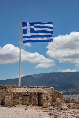 Athens Acropolis, Greece. Greek flag waving on pole, against blue sky background, spring sunny day, vertical photo.の写真素材