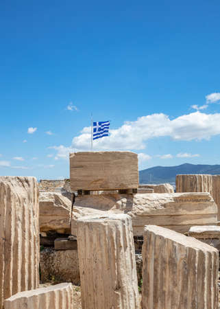 Athens Acropolis, Greece. Greek flag waving on pole, ancient column remains against blue sky background, spring sunny day.の写真素材