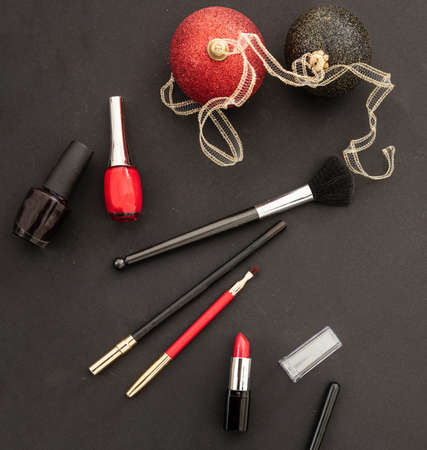 Makeup xmas party concept. Make up products and christmas balls red and black flat lay against black background. New years eve preparationの写真素材