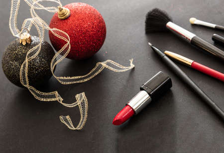 Makeup xmas party concept. Make up products and christmas balls red and black against black background. New years eve preparationの写真素材