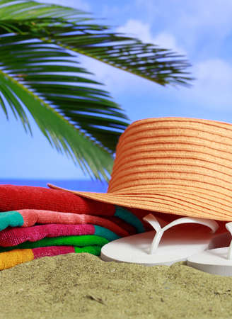 Summer holidays by the sea concept. Flip flops, towel and straw hat on a sandy beach. Blue sea and sky background. Vertical photo, closeup view.の写真素材