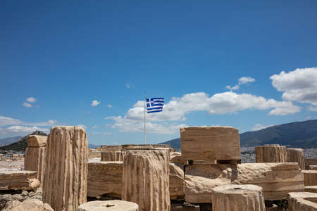 Athens Acropolis, Greece. Greek flag waving on pole, ancient column remains against blue sky background, spring sunny day.の写真素材
