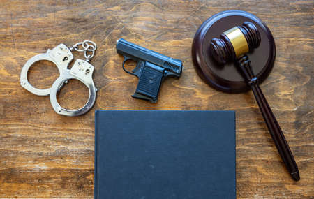Law, crime, punishment concept. Judge gavel, handgun, handcuffs and a blank cover legal book on wooden desk background, top view, copy space.の写真素材