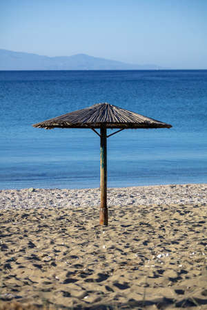 Straw umbrella on an empty sandy beach. Blue sea and sky background, sunny spring day, verticalの写真素材