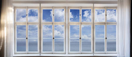 View of calm sea and blue sky background through old window concept. Vintage white window pane with frame, transparent glasses, handles and sill. Banner.の写真素材