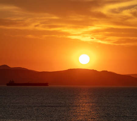 Sunset orange cloudscape over sea water. Dramatic magical sunrise seascape in Aegean sea Greece. Twilight, dawn background. Dark island land and orange cloudy skyの写真素材