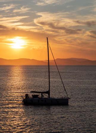 Sailing at sunset in the Aegean sea, Greece. Sailboat on calm sea and orange sky background,の写真素材