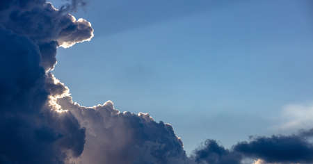 Cloudscape. Heavy dark clouds on sky background. Fluffy clouds cover the sun and the sky except a clear blue empty area. Card, wallpaper, copy spaceの写真素材
