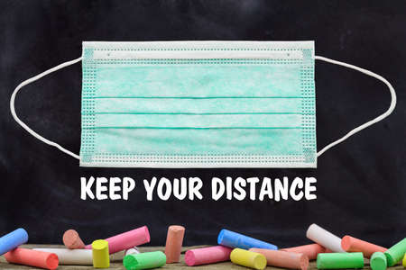 KEEP YOUR DISTANCE text and blank protective mask against blackboard with colorful chalks background, Coronavirus spread in school prevention measure, sign templateの写真素材