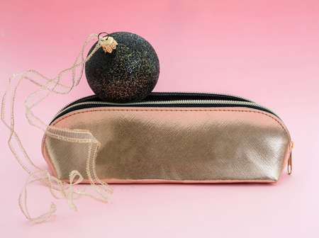 Make up xmas party concept. Cosmetic make up bag gold and christmas decoration against pink color...