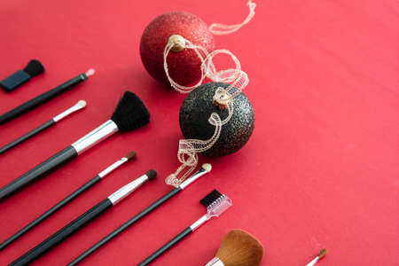 Makeup xmas party concept. Make up brushes set and christmas balls against red background, top view. Professional tools for make upの写真素材