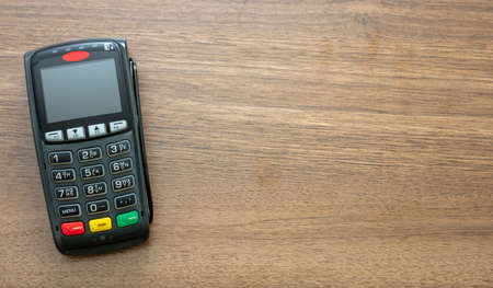 POS terminal isolated on wooden background, top view.Terminal cash register machine for contactless payment with credit card. Banking equipment, NFC.の写真素材