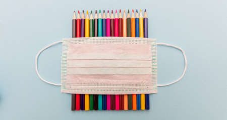 Back to school, coronavirus days. Medical protective mask blank white and colored pencils on pastel...