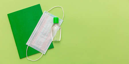 Back to school, coronavirus days. Medical protective mask, hand sanitizer gel and school notebook on pastel green color background, top view, Template, copy spaceの写真素材