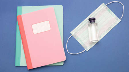 Back to school, coronavirus days. Medical protective mask, hand sanitizer gel and school notebooks on blue color background, top view, Template, copy spaceの写真素材