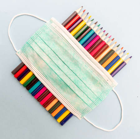 Back to school, coronavirus days. Medical protective mask blank and colored pencils on pastel blue color background, top view, Template, copy spaceの写真素材