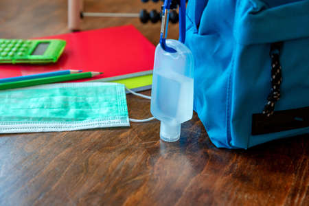 School, coronavirus days. Hand sanitizer gel and school bag backpack on wooden desk background,...