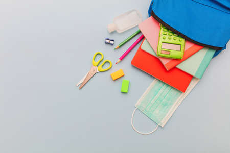 School, coronavirus days. School supplies, medical mask and sanitizer gel out of a school bag, pastel blue color background, top view, copy spaceの写真素材