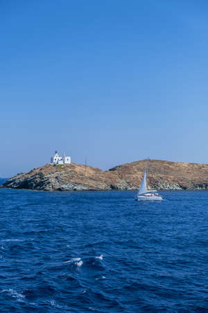 Greece, Kea Tzia island. Lighthouse on a cape, sailboat sailing, clear blue sky and rippled sea water backgroundの写真素材