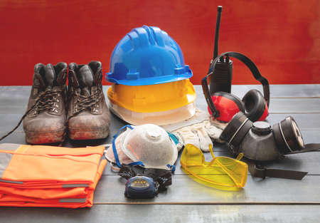Work safety protection equipment. Industrial protective gear on wooden table, red color background....
