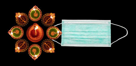 Coronavirus and Diwali 2020 concept. Face protective mask and illuminated diyas against black background. COVID19 spread prevention measureの写真素材