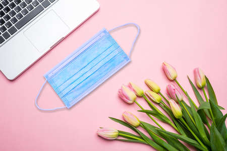 Business office female desk, coronavirus days. Protective face mask, tulips and laptop, pink color woman background, copy space. COVID19 disease prevention,の写真素材