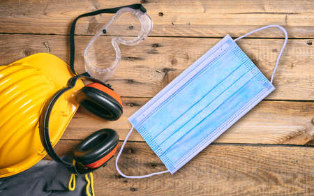 Work safety and coronavirus. Protective face mask and construction site safety tools, wooden table background.  COVID19 disease prevention.の写真素材
