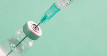 Vaccine, coronavirus vaccination, covid-19 flu prevention, immunization concept. Vial dose and medical syringe, drug medicine shot injection, pastel green background, closeup.の写真素材