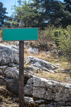 Green blank signboard mockup on wooden pole, forest mountain  nature background. Path, trail information template for hiking, Copy space.の写真素材