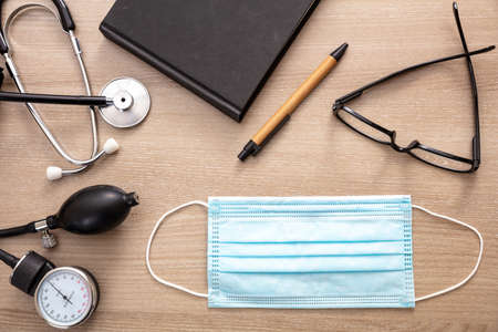 Medical stethoscope sphygmomanometer and protective mask on cardiologist doctor office desk. Coronavirus protection, healthcare concept, top viewの写真素材