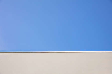 Beige color painted empty wall in contrast of clear blue sky background, texture. Copy space, ad template, low angle view.の写真素材
