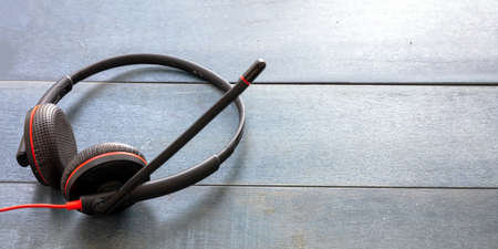 Call center and home office concept. Customer service support, help desk, communication. Headset black with red details on blue wooden office desk, copy spaceの写真素材