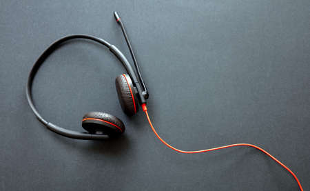 Customer service support, help desk, communication. Call center and home office concept. Headset black with red details on black background, top view, copy spaceの写真素材